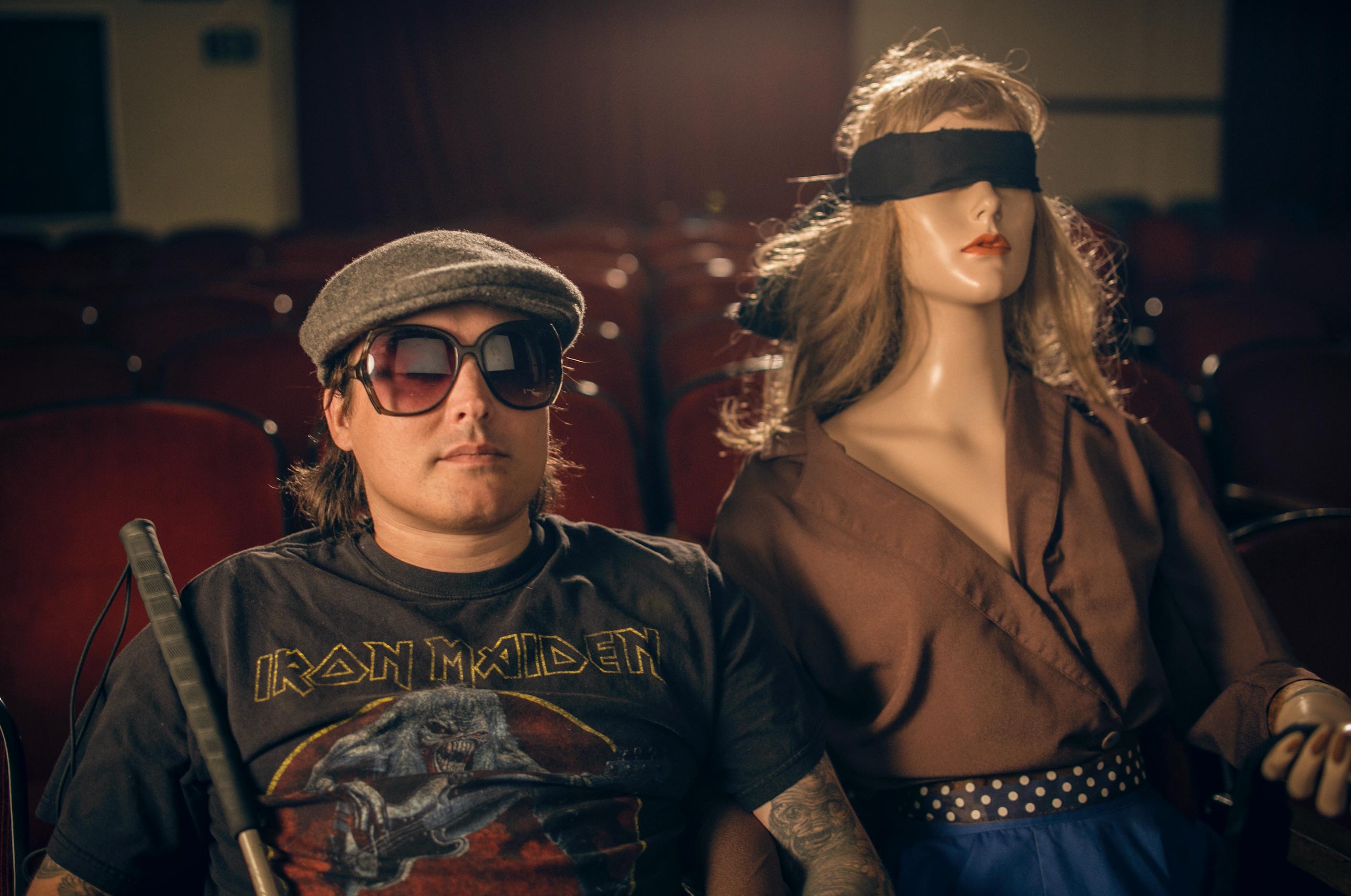 Brendan Patrick in an empty movie theater, with a blindfolded mannequin in the row behind him.